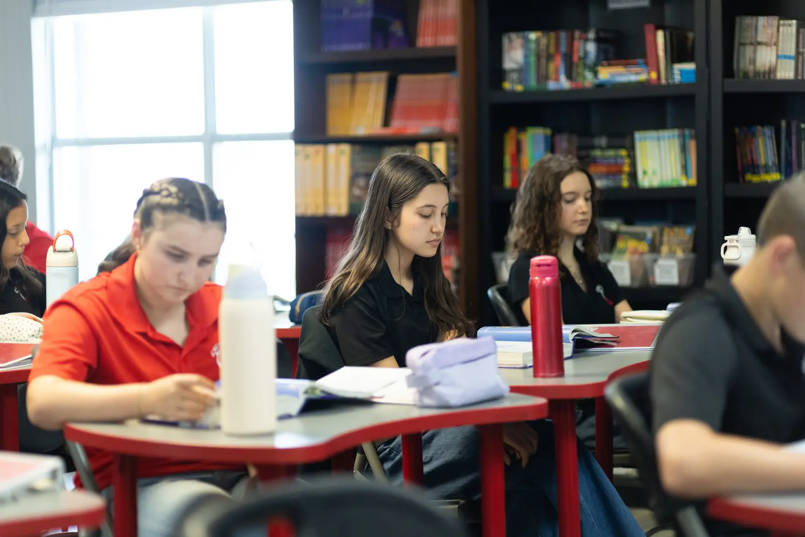 Students reading and studying in a library with bookshelves