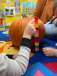 A child's hand measuring a pumpkin with measuring blocks.